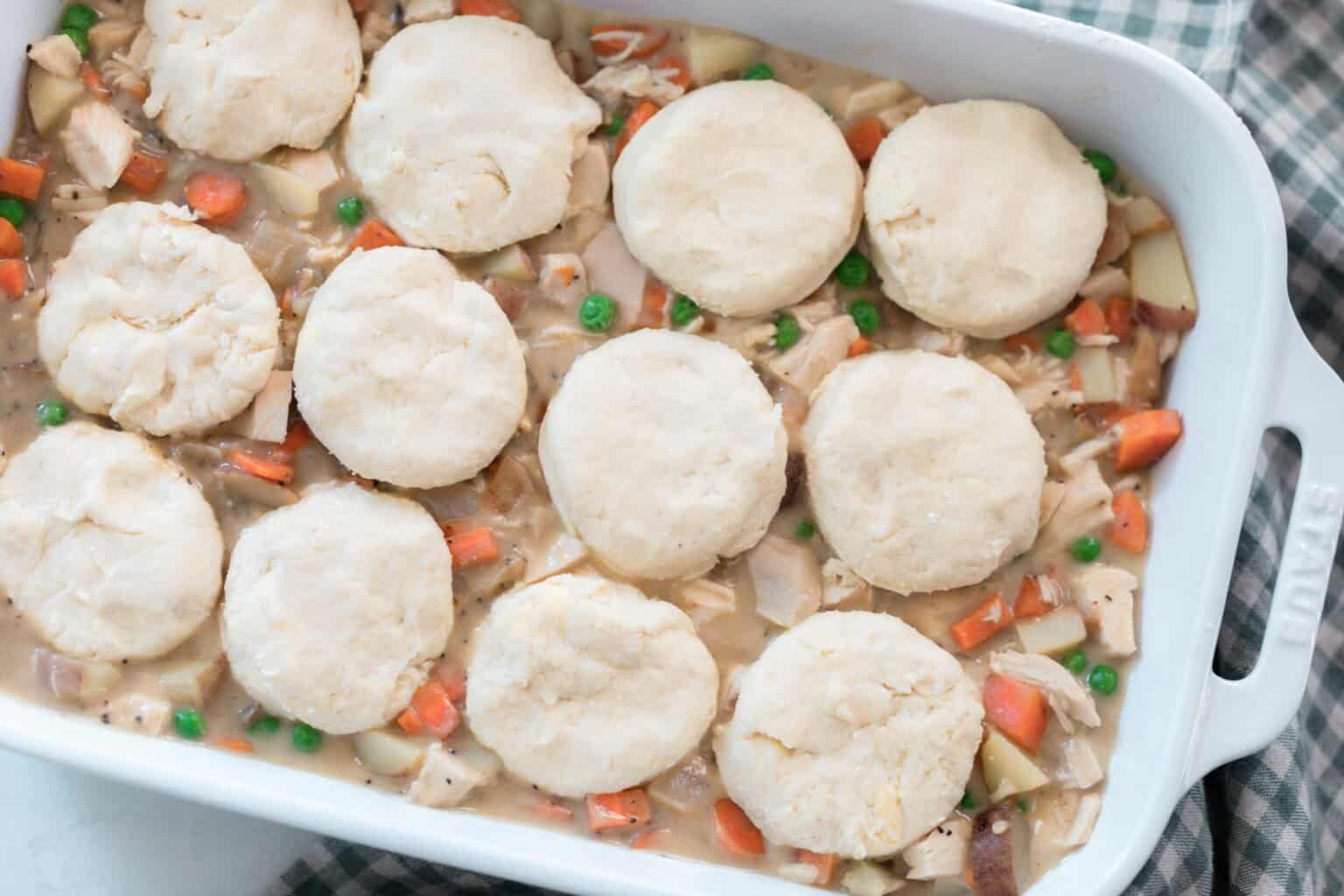 Raw biscuits on top of chicken pot pie filling in a white baking dish.