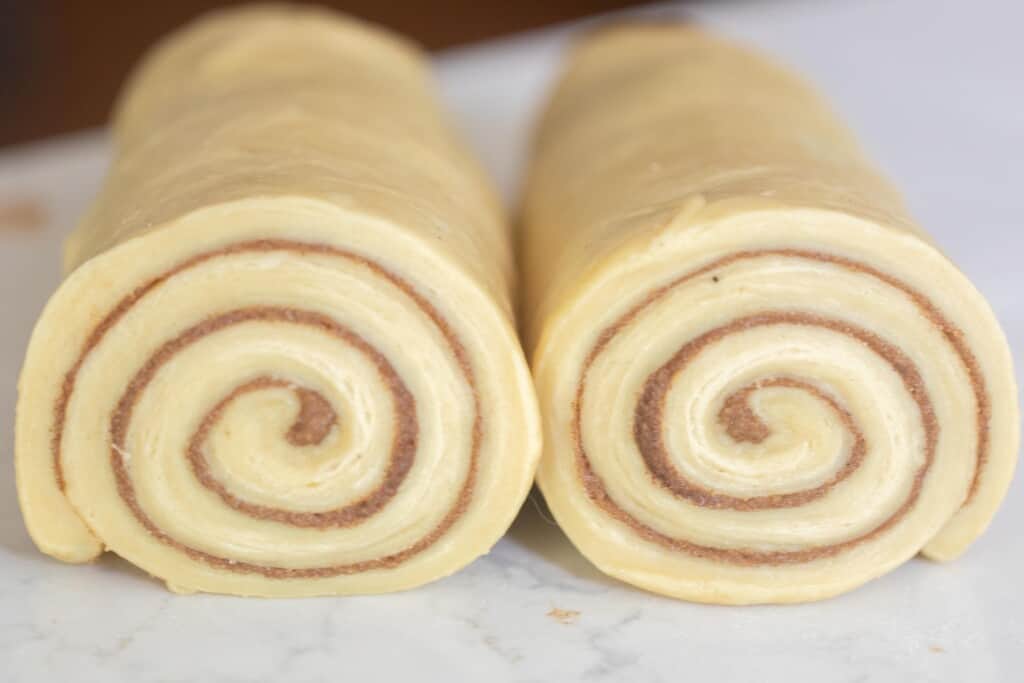 cinnamon roll dough rolled up with the cinnamon sugar filling on a white countertop