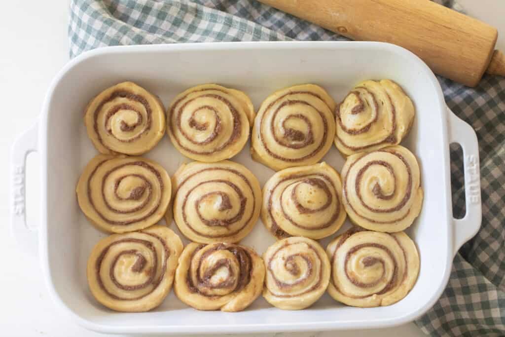 unbaked sourdough cinnamon buns in a white baking dish on top of a green and white checked towel