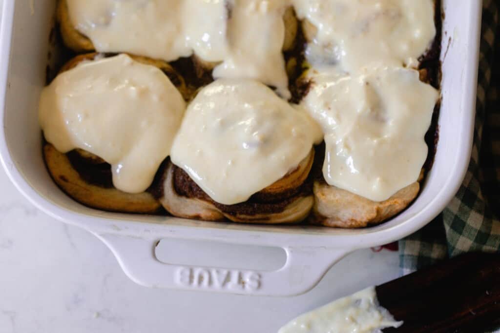 overhead photo of a half a baking dish of sourdough cinnamon rolls topped with cream cheese topping