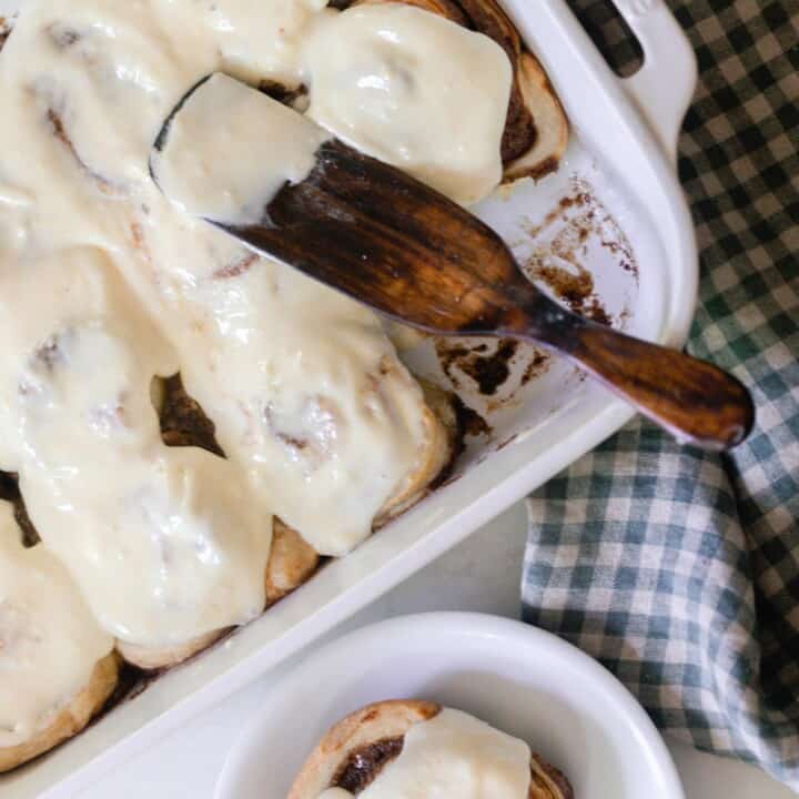 overhead photos of sourdough cinnamon rolls covered in a cream cheese icing in a white baking dish with a white plate with a cinnamon roll to the right