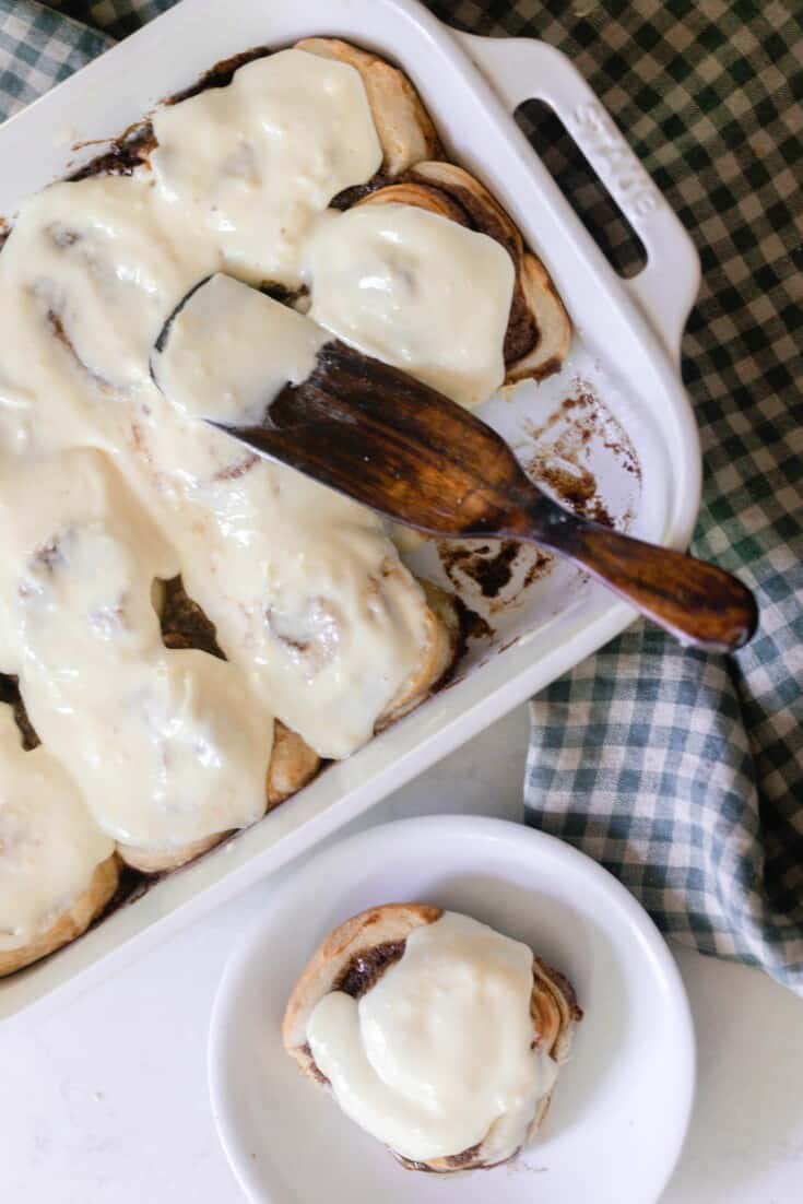 overhead photos of sourdough cinnamon rolls covered in a cream cheese icing in a white baking dish with a white plate with a cinnamon roll to the right