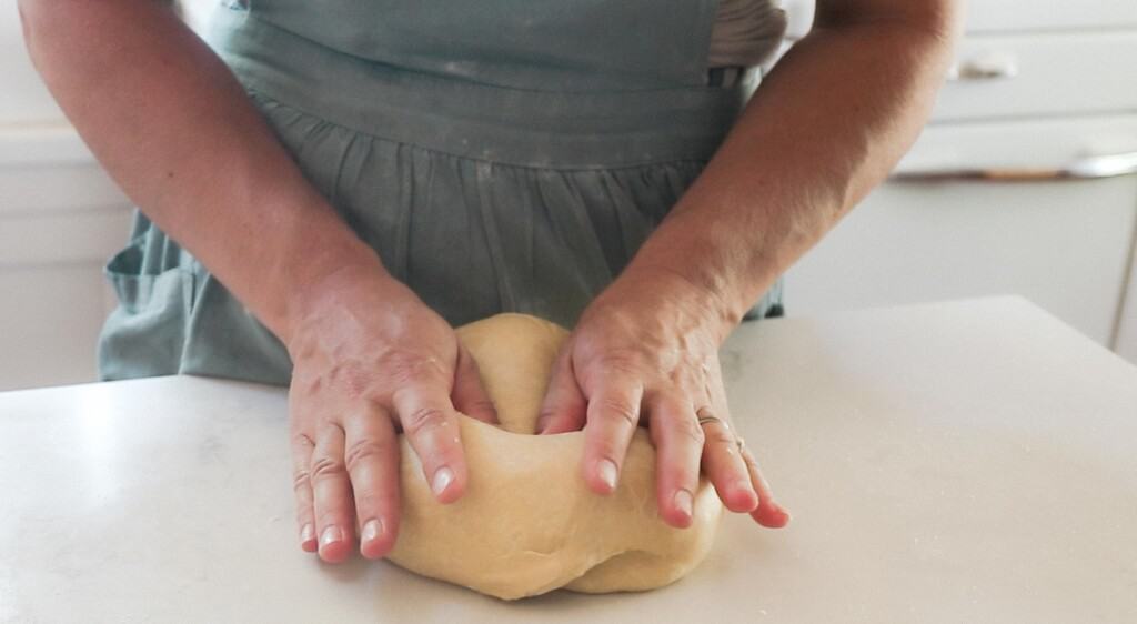 hands kneading dough on a white countertop