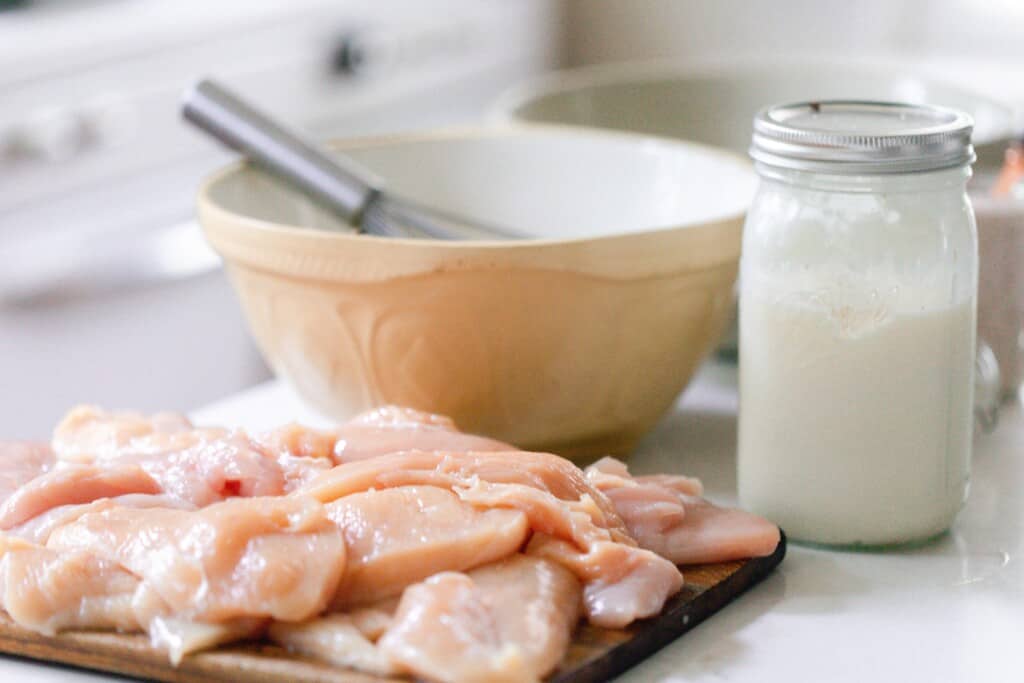 chicken sliced on a cutting board with bowls and jars in the background