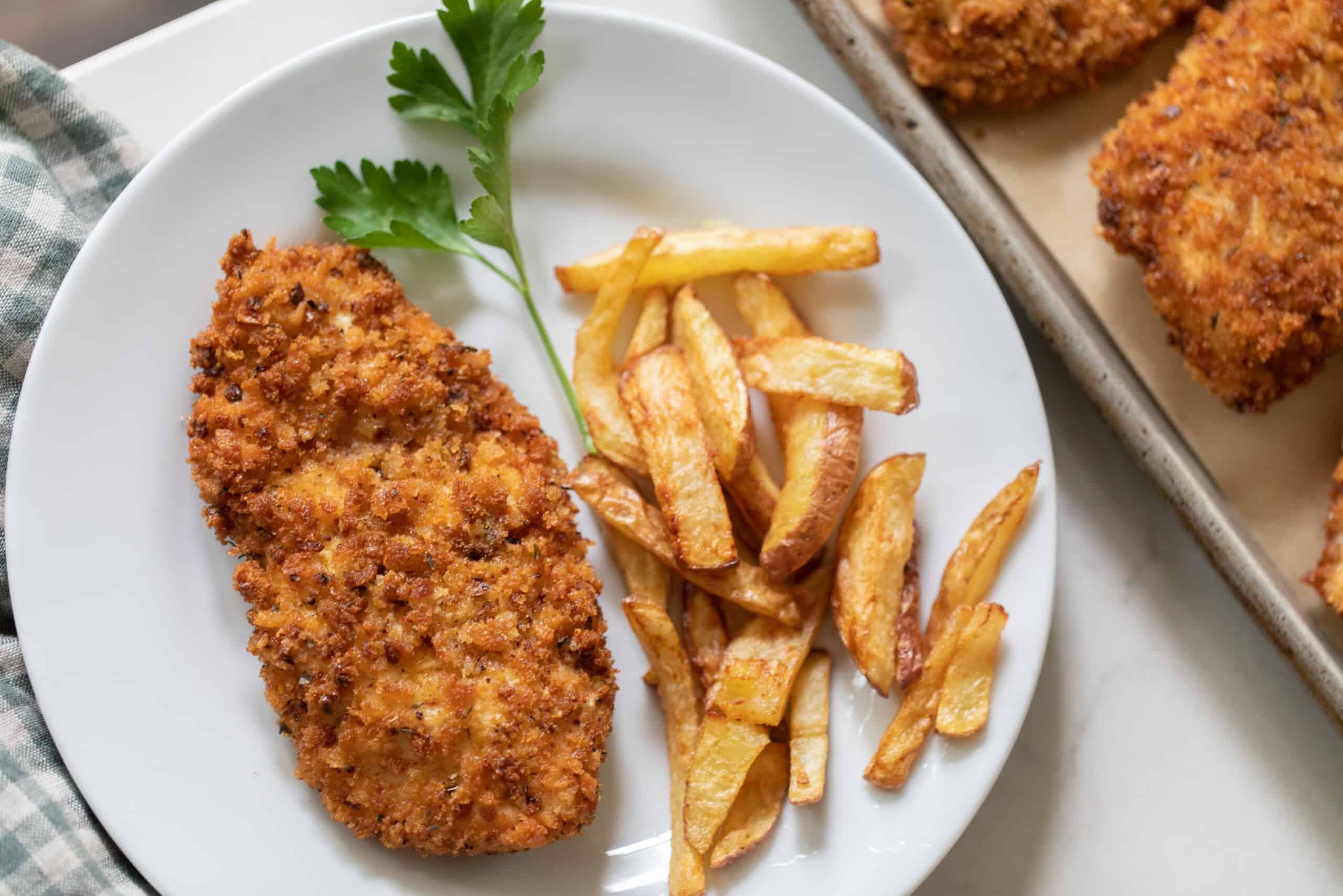 overhead photo of sourdough fried chicken with French fries and a sprig of parsley on a white plate