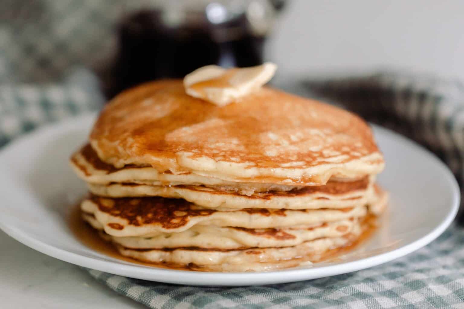 A stack of sourdough pancakes topped with a pat of butter and maple syrup on a white plate.