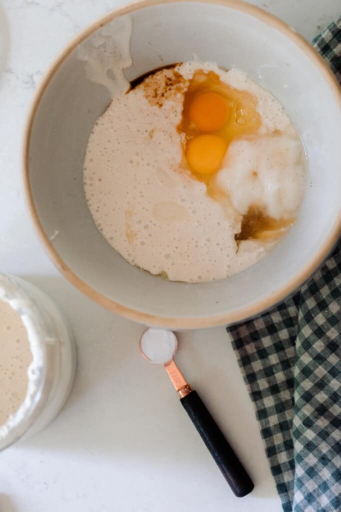 sourdough starter, oil, and eggs in a bowl with a measuring spoon of baking soda in front of the bowl