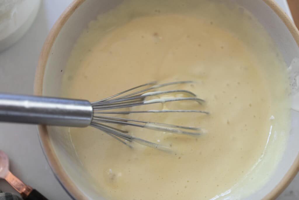 sourdough waffle batter with a whisk in it in a stoneware bowl