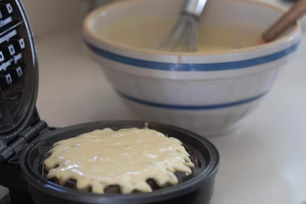 sourdough waffle batter poured into a waffle iron with a bowl in the background