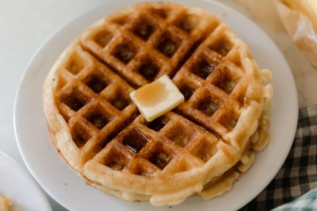 overhead photo of a sourdough waffle topped with syrup and butter on a white plate