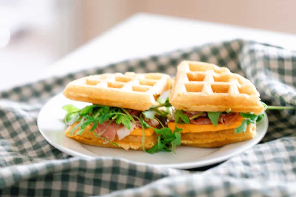 a sourdough cheddar waffle made into sandwiches with lettuce, tomato, cheese, and ham