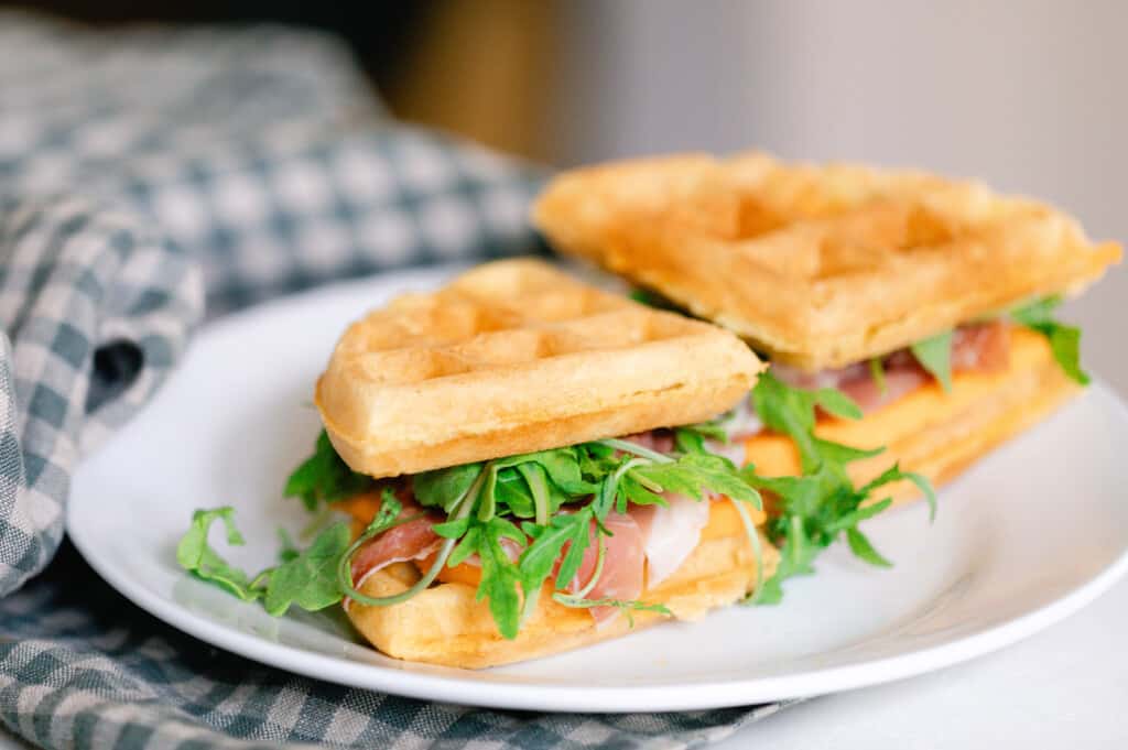 sourdough cheddar waffle sandwiches with lettuce, tomato and ham on a white plate on a blue plaid napkin