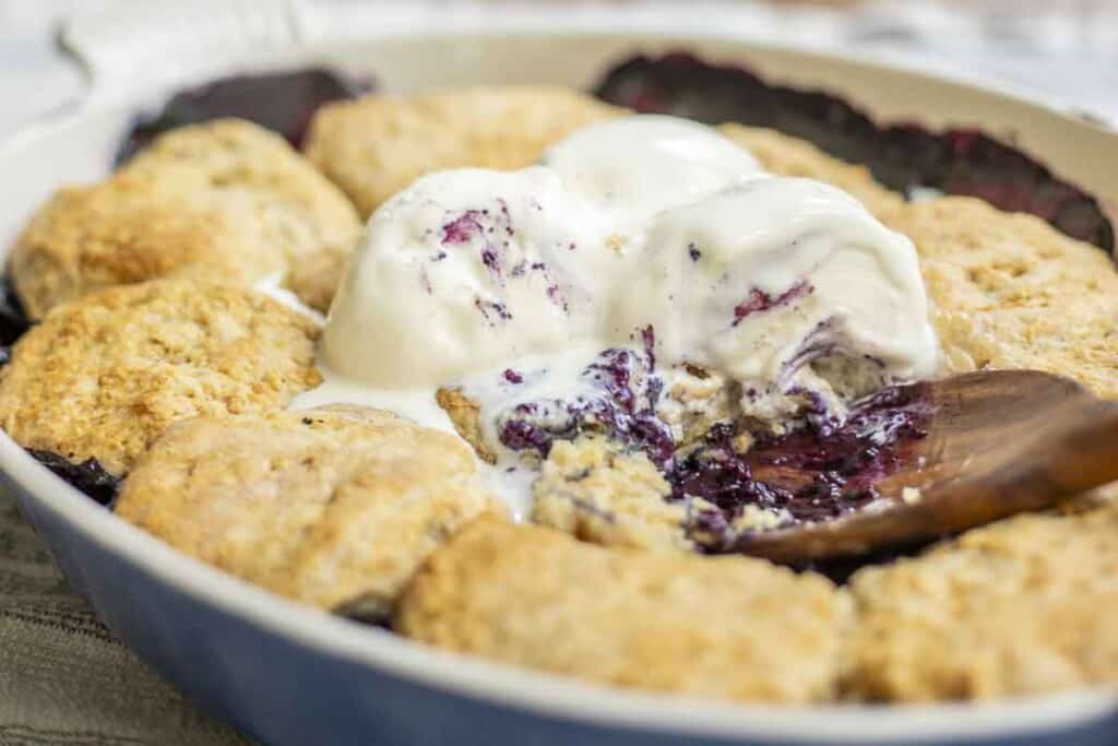 sourdough blueberry cobbler topped with ice cream with a wooden spoon in it