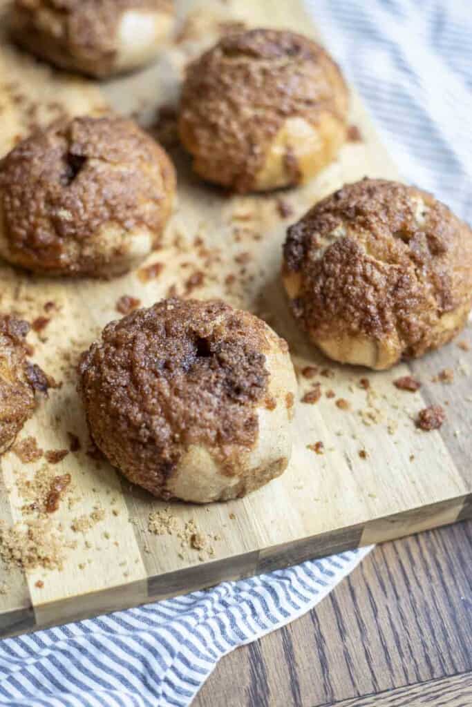 5 sourdough cinnamon crunch bagels on a wood cutting board on a white and blue stripped towel