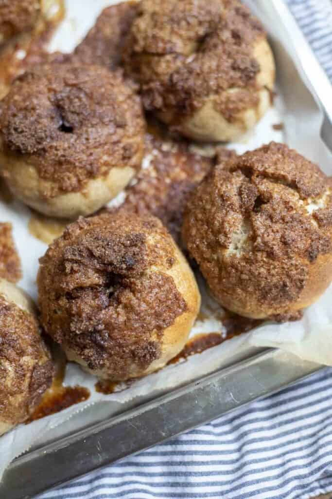 four sourdough cinnamon crunch bagels on a parchment lined backing sheet on a blue stripped towel