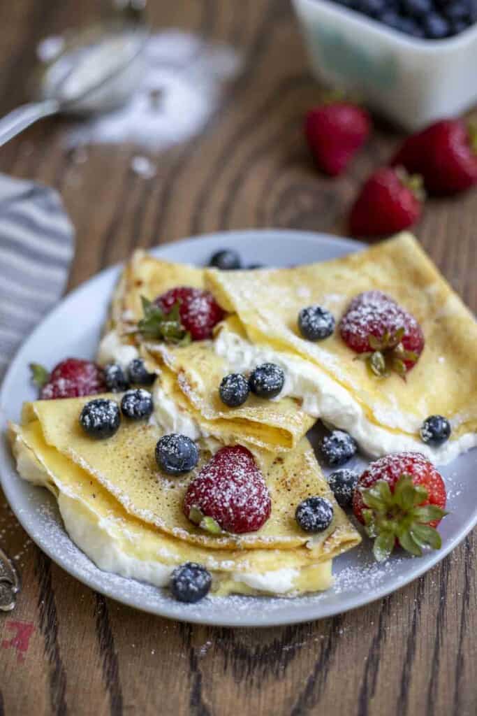 three sourdough crepes filled with whipped cream and berries on a gray plate
