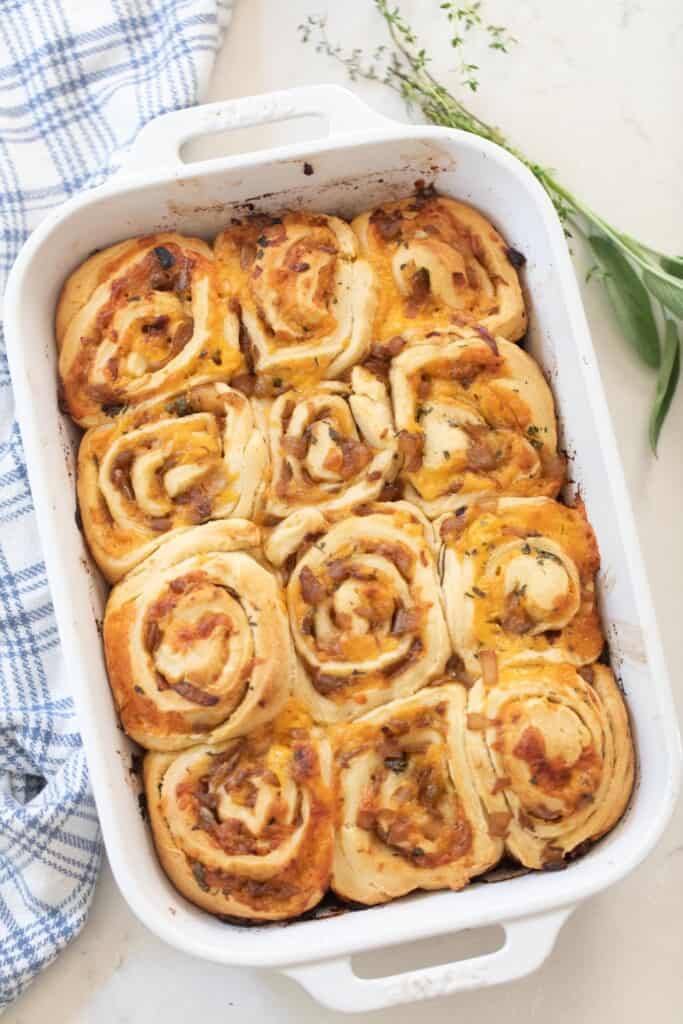 overhead photo of sourdough herb and cheese rolls in a white baking dish on a white countertop with a white and blue plaid towel