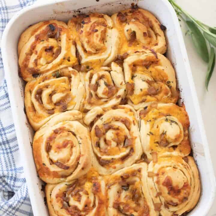 overhead photo of sourdough herb and cheese rolls in a white baking dish on a white countertop with a white and blue plaid towel