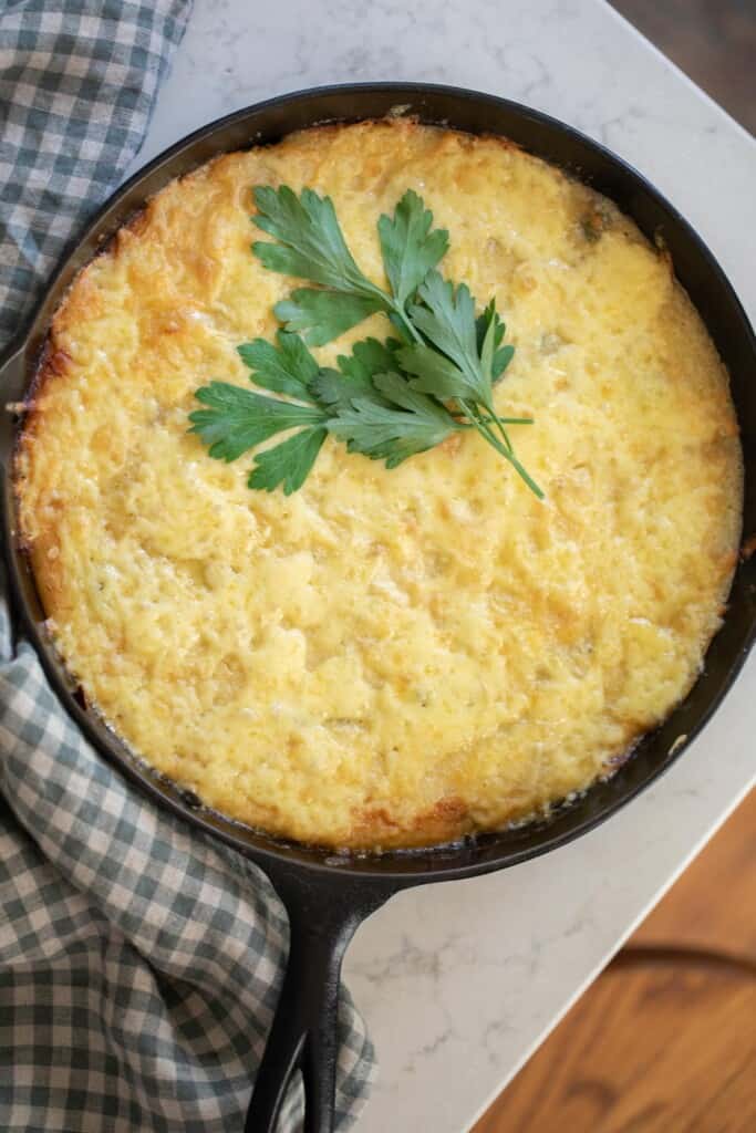 overhead photo of sourdough skillet topped with cheese and parsley in a cast iron skillet on white towel