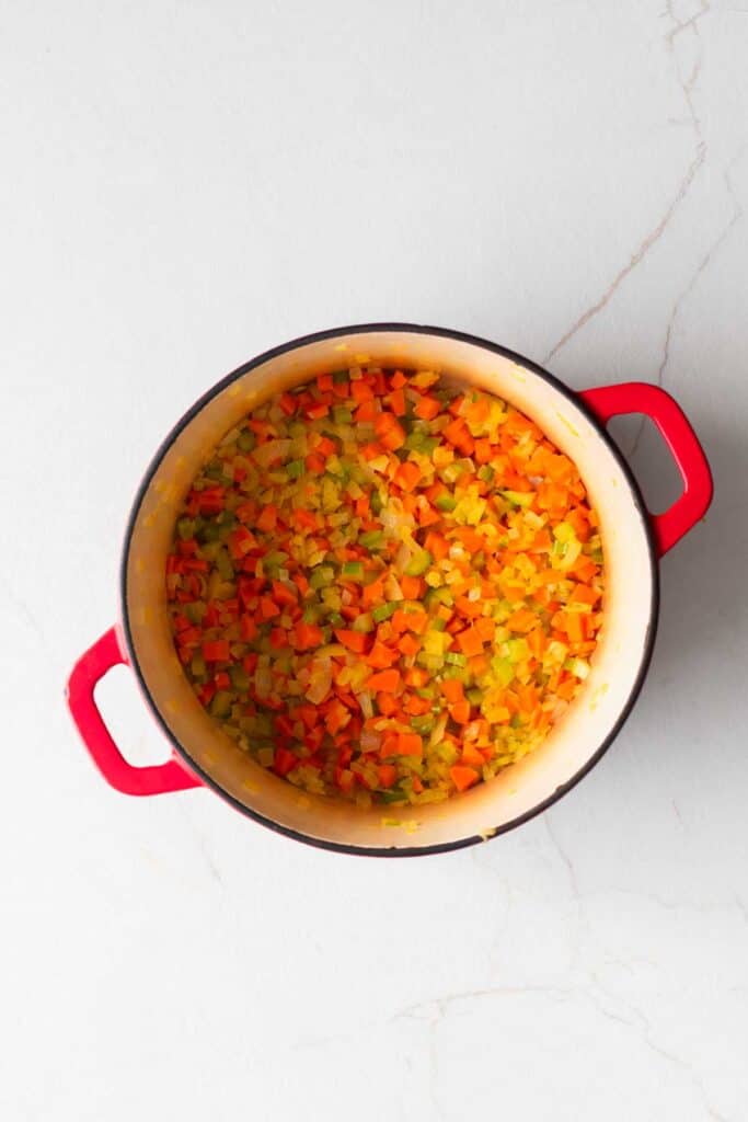 A dutch oven with vegetables chopped.