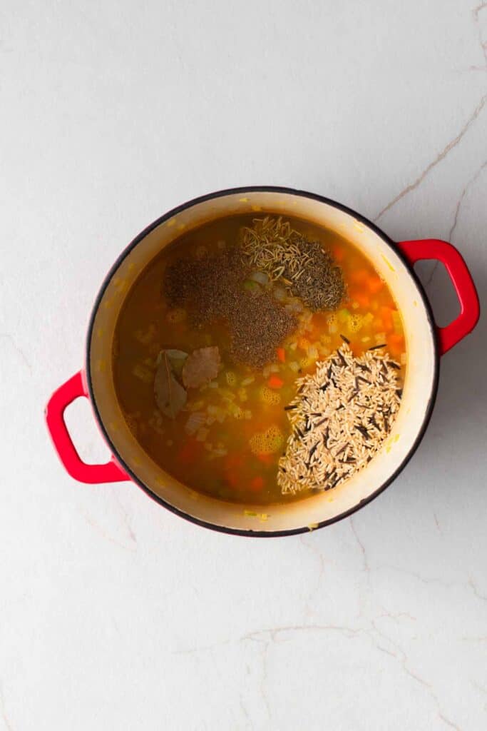 A dutch oven with chopped vegetables, broth, and seasonings.