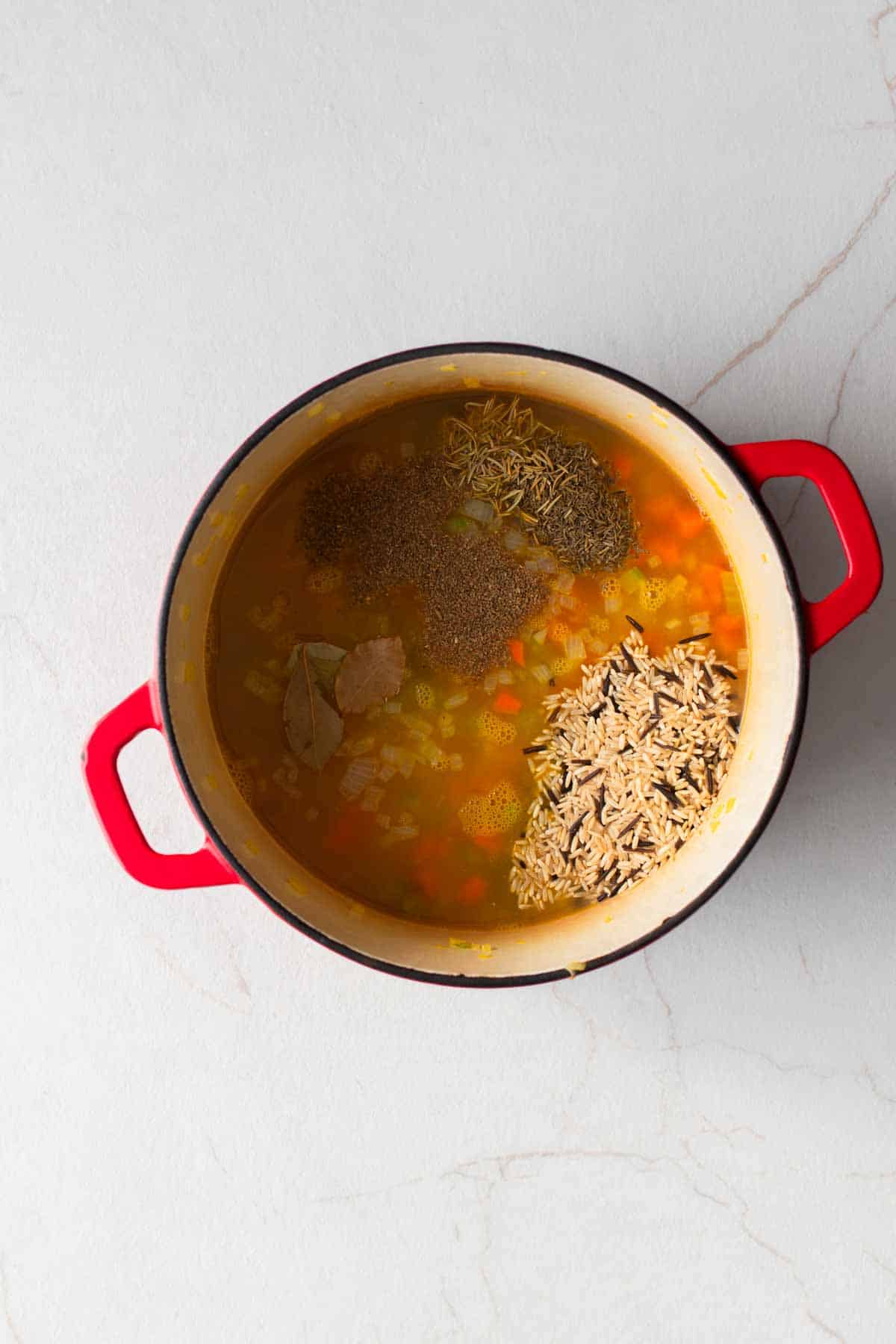 A dutch oven with chopped vegetables, broth, and seasonings.