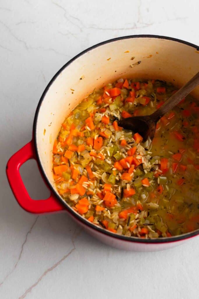 Dutch oven with a wooden spoon stirring in ingredients. 