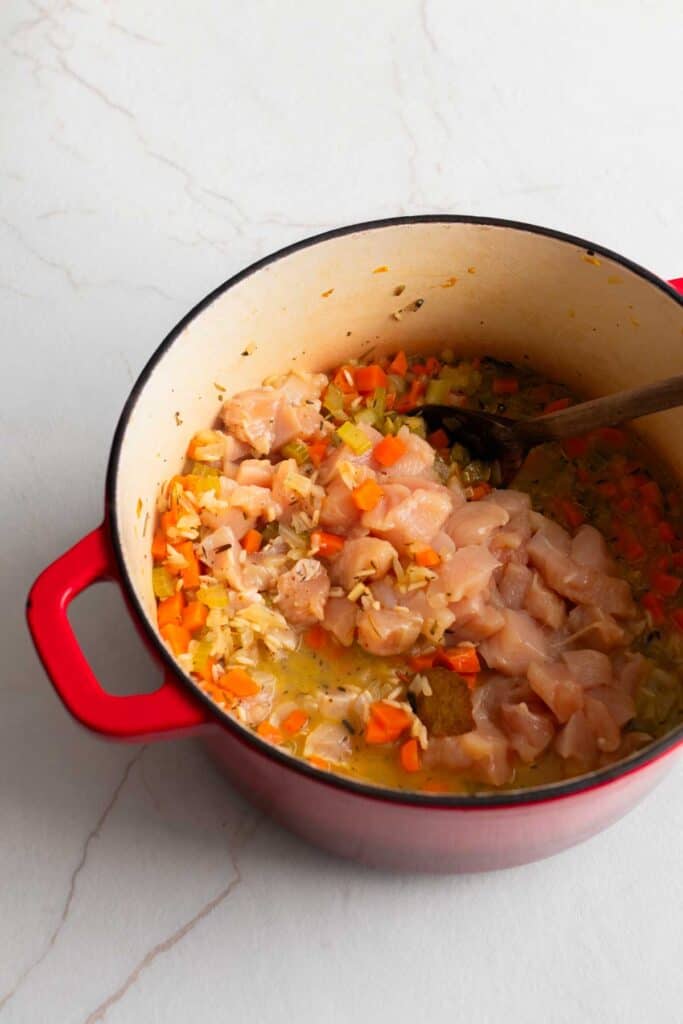 A dutch oven with vegetables, rice, seasonings, and cubed chicken.