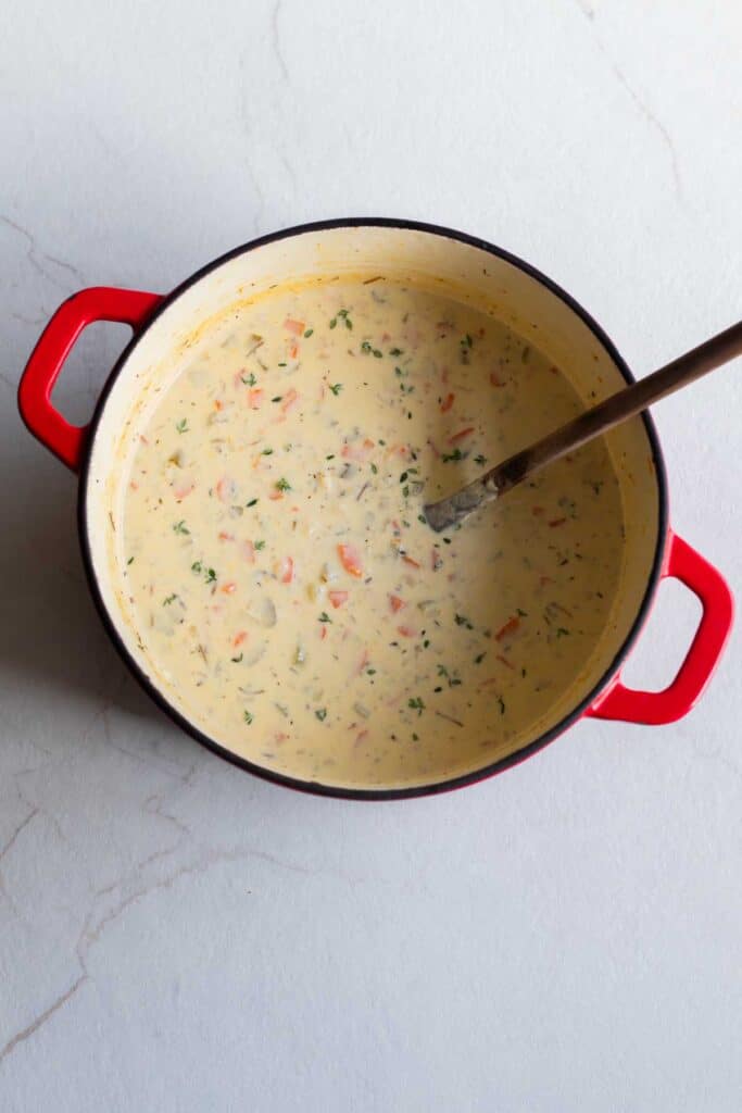 A dutch oven with chicken and wild rice soup with a large spoon sticking out of it.
