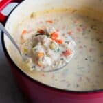 A dutch oven with chicken and rice soup being ladled out.