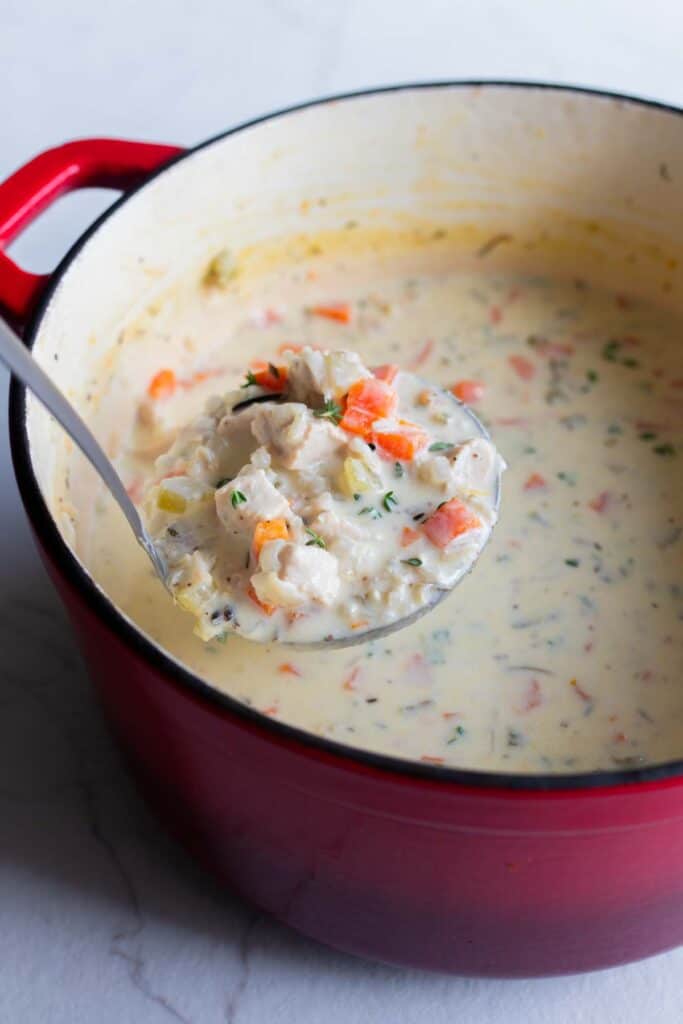 A dutch oven with chicken and rice soup being ladled out. 