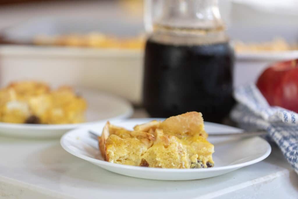 sourdough French toast casserole on a white plate with a glass jar of maple syrup in the background