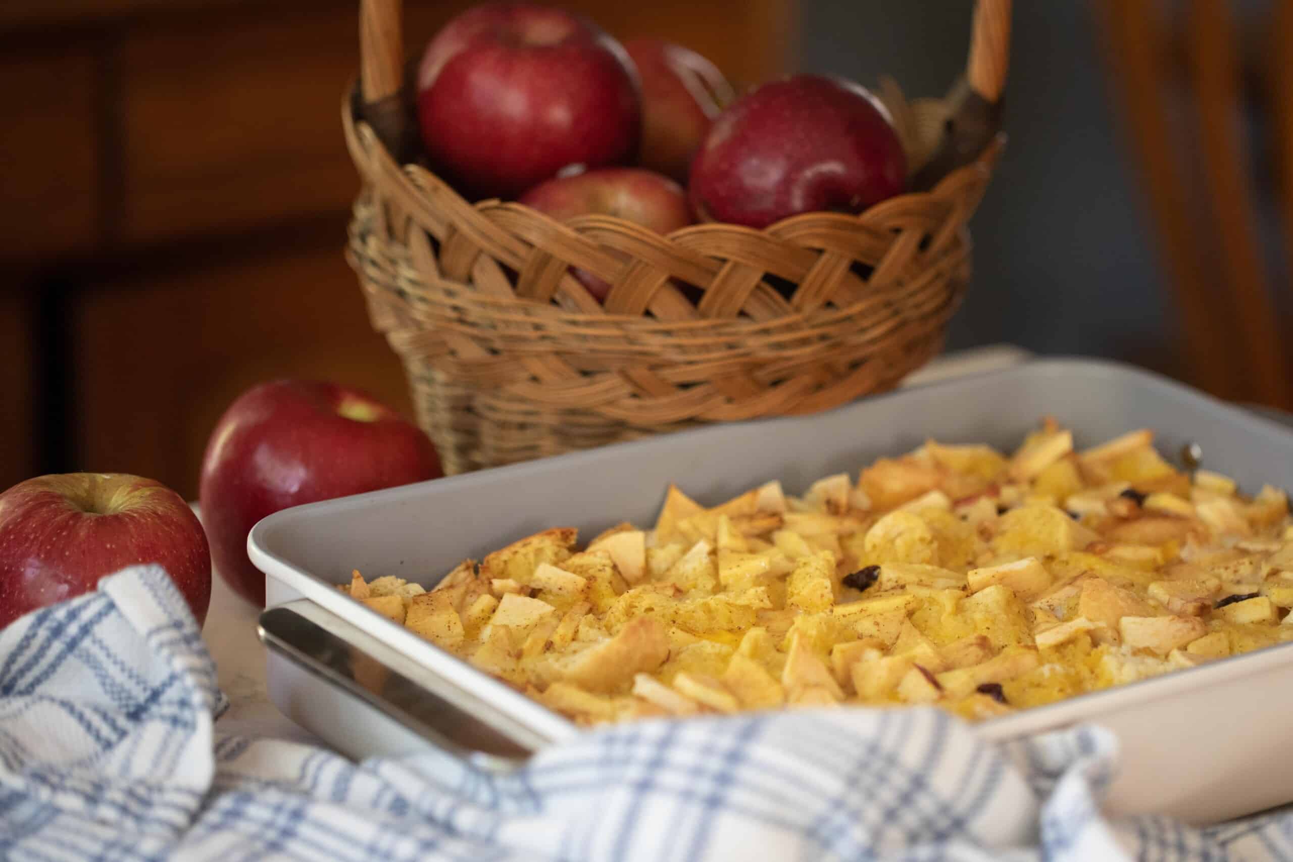 sourdough French toast casserole with raisins and apples in a baking dish with a basket of apples in the background
