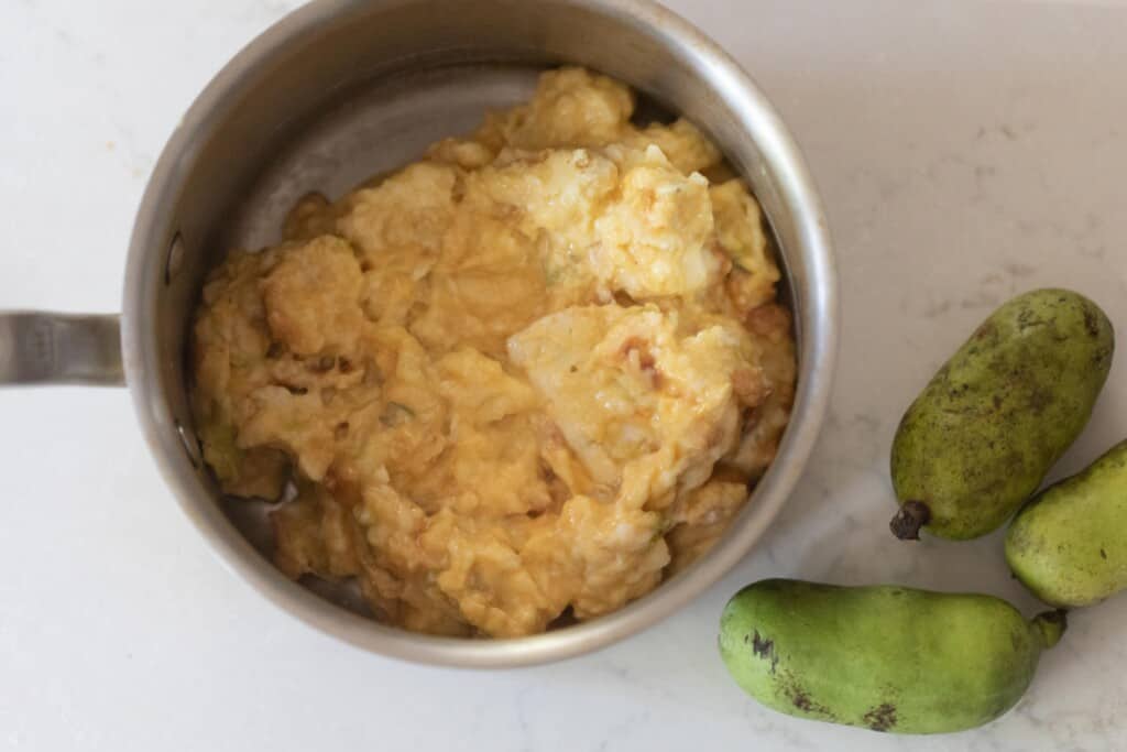 pawpaw pulp in a saucepan on a white countertop with 3 pawpaws to the right