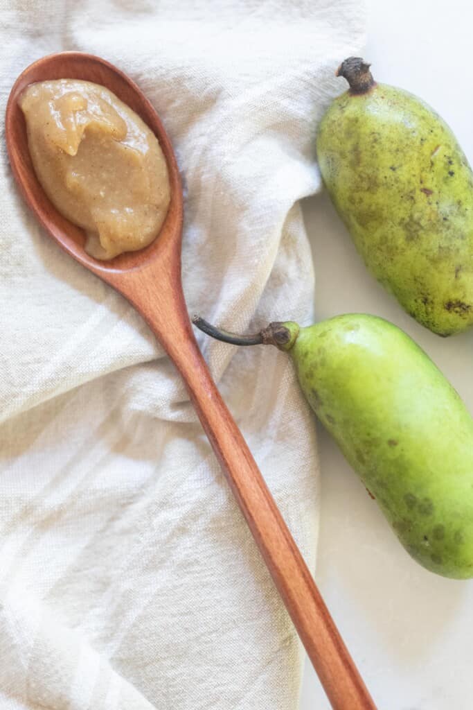 pawpaw jam on a wooden spoon on a white towel with fresh pawpaws to the right