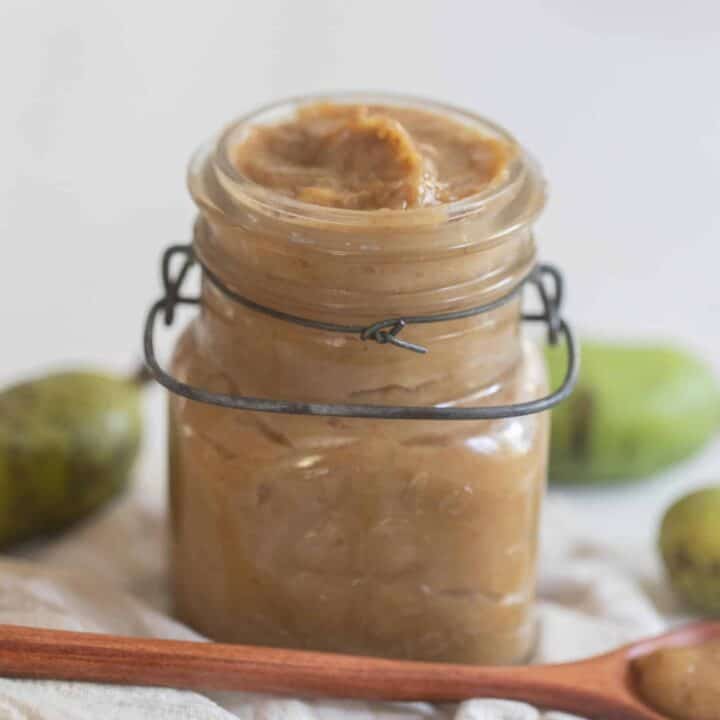 pawpaw jam in a glass swing top jar with pawpaws in the background and a wooden spoon in front of the jar
