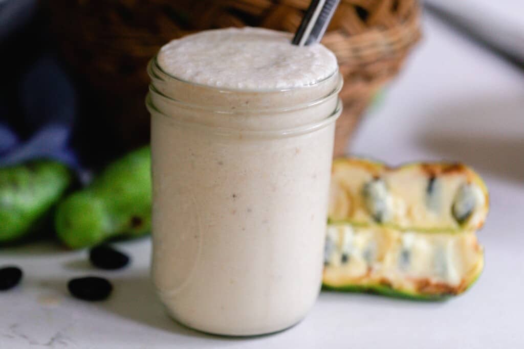 pawpaw and banana smoothie in a mason jar with metal straw. More pawpaws are in the background