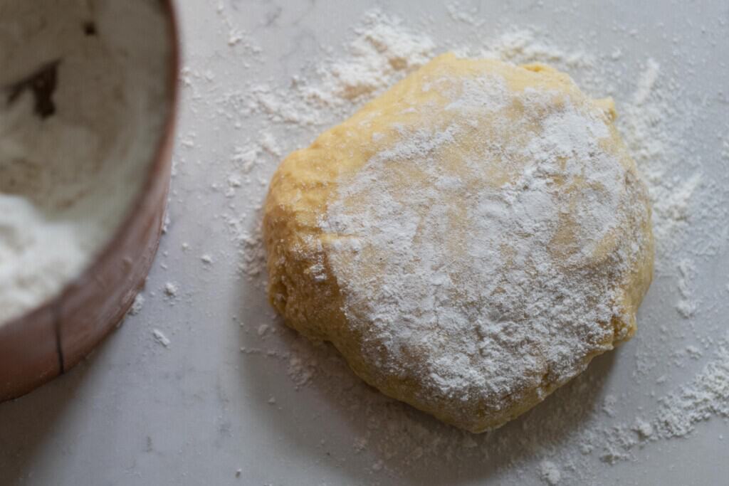 sourdough noodle dough in a disk covered with flour on a white countertop