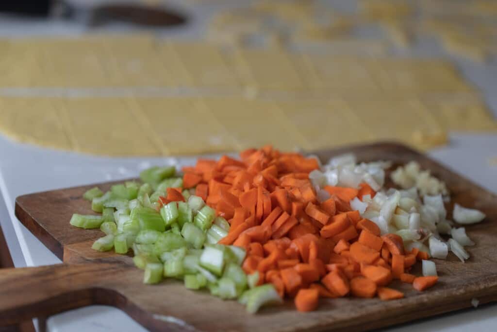 diced celery, carrots, and onion on a wood cutting board