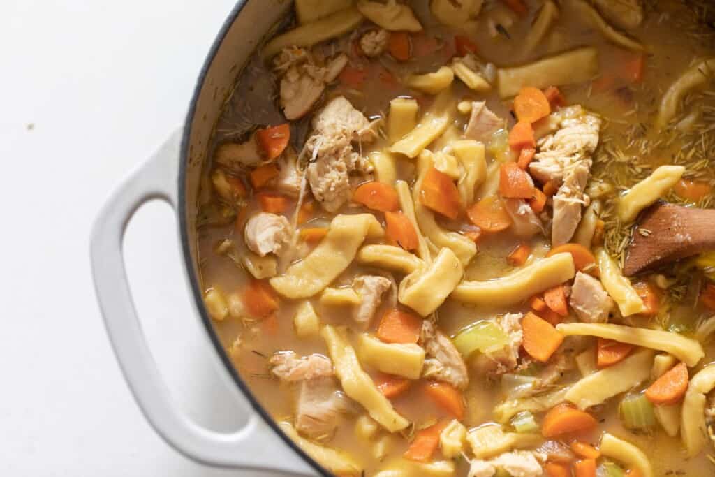 overhead photo of chicken noodle soup with homemade noodles in a white dutch oven