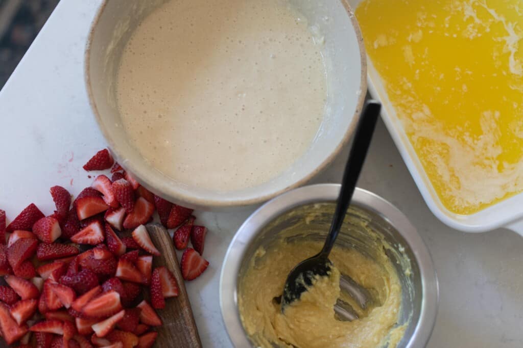 bowls with different ingredients to make sourdough cobbler with strawberries chopped on a white countertop