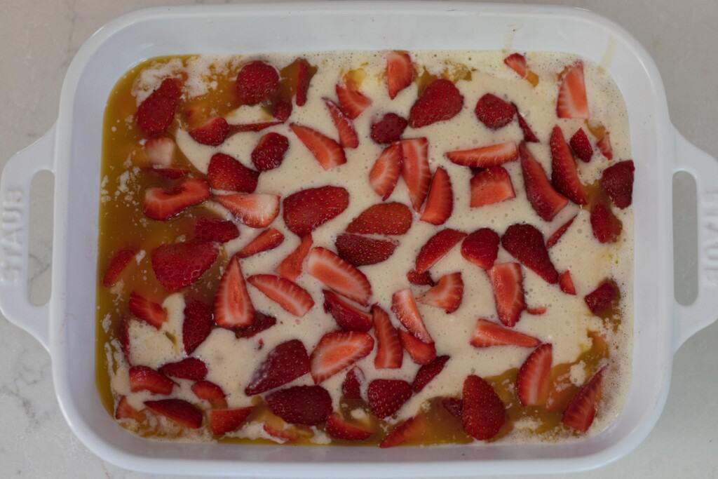 strawberries arranged on top of melted butter and sourdough batter in a white baking dish