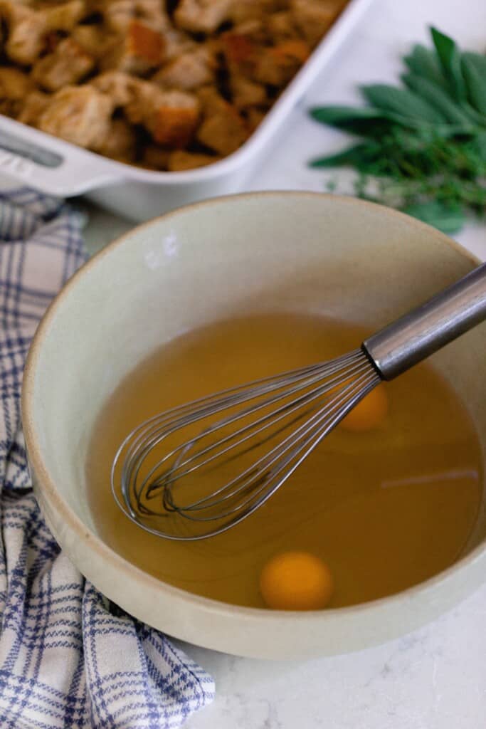 eggs and broth in a stoneware bowl with fresh herbs and baking dish of toasted bread in the background