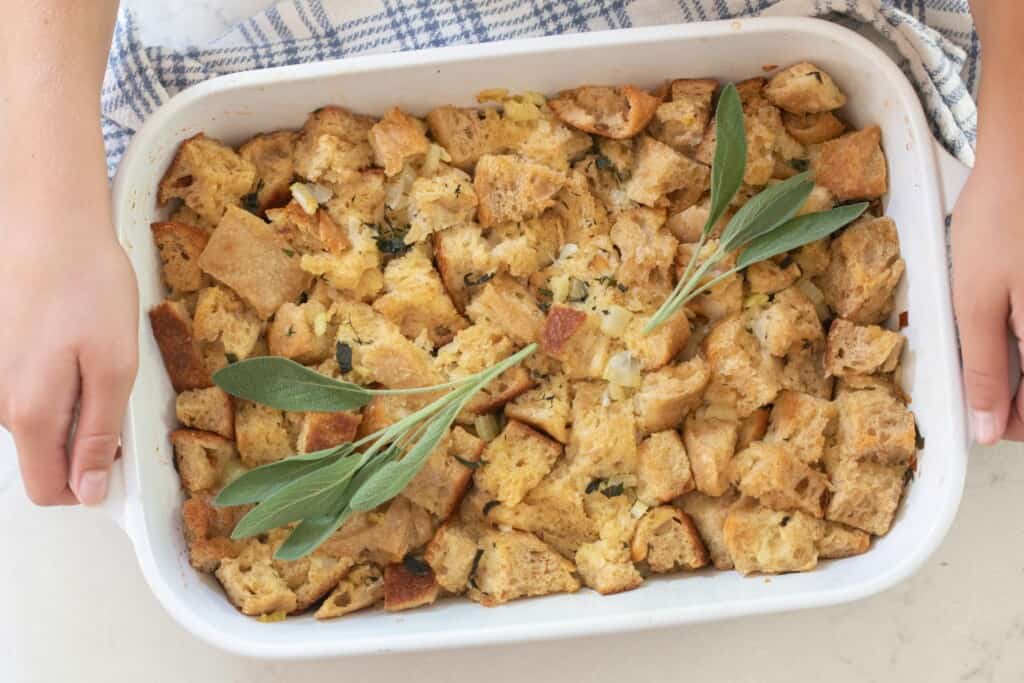 hands holding a white baking dish full of homemade sourdough stuffing