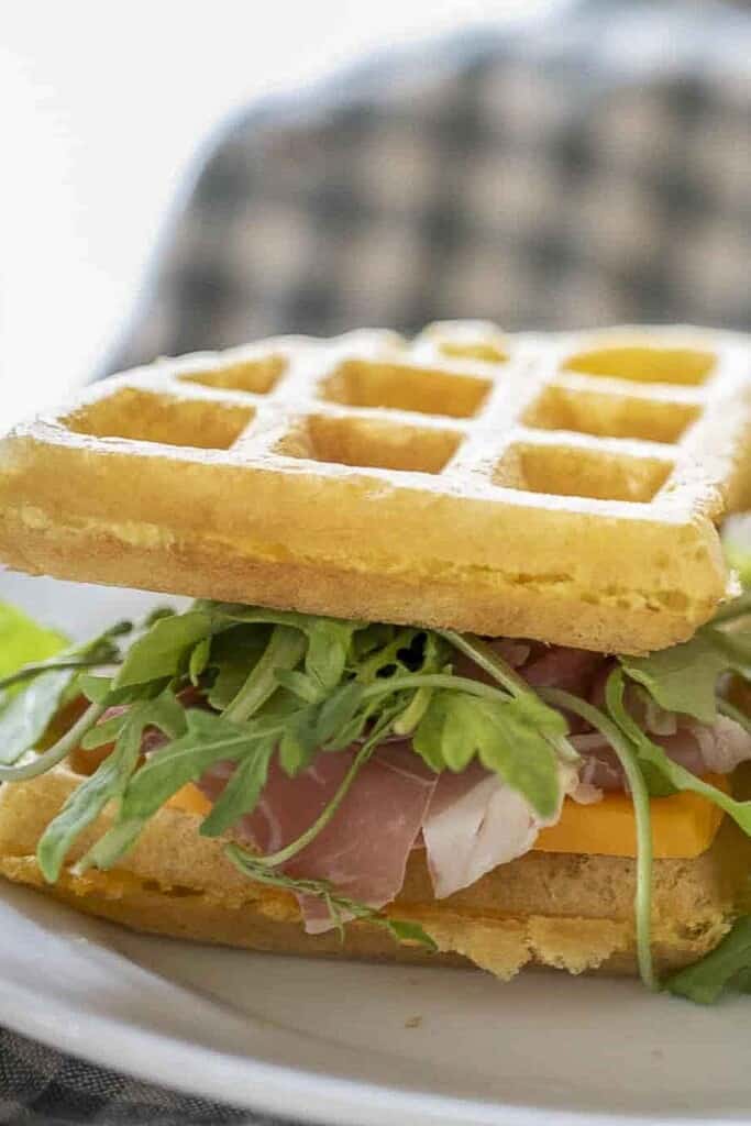 close up picture of a sandwich made with sourdough cheddar waffles as the bread, lettuce, cheese, and ham
