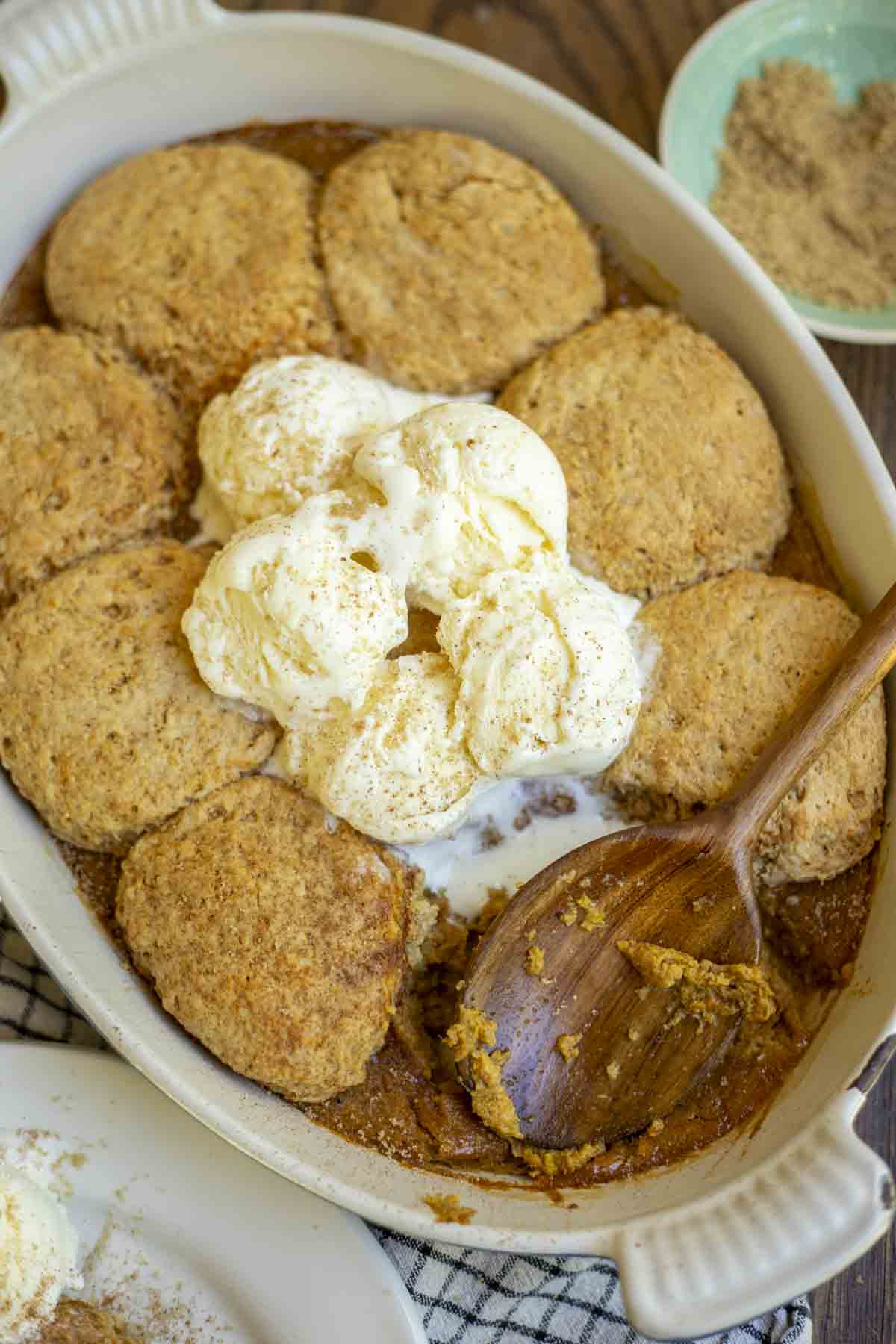 overhead photo of sourdough pumpkin cobbler topped with vanilla ice cream in a baking dish. A teal bowl with brown sugar is in the background
