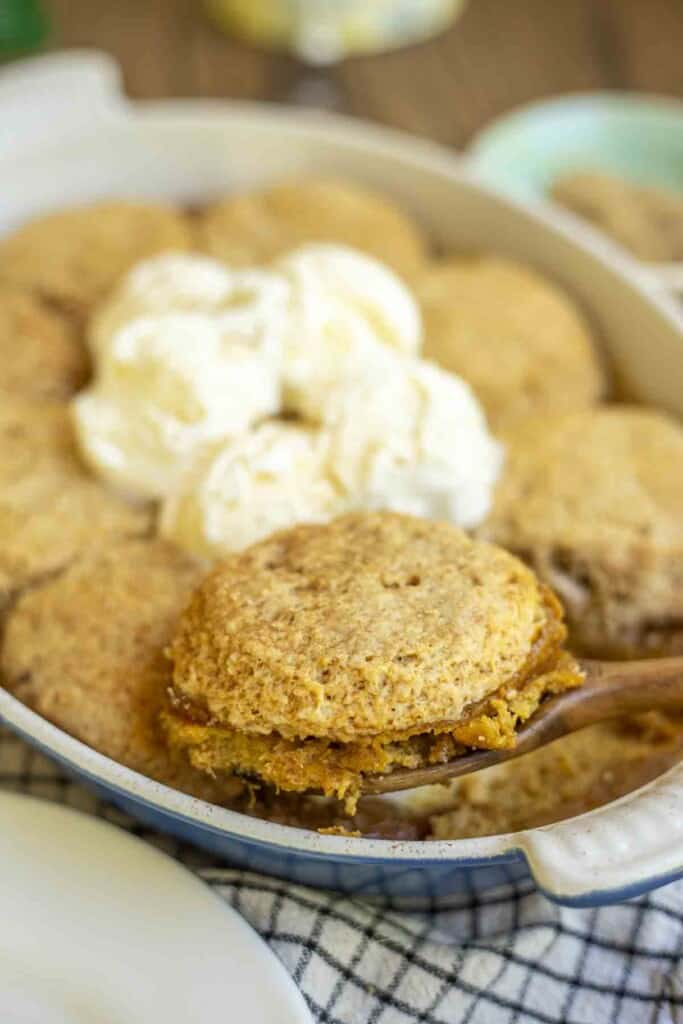 a wooden spoon taking out sourdough pumpkin cobbler topped with ice cream from a baking dish