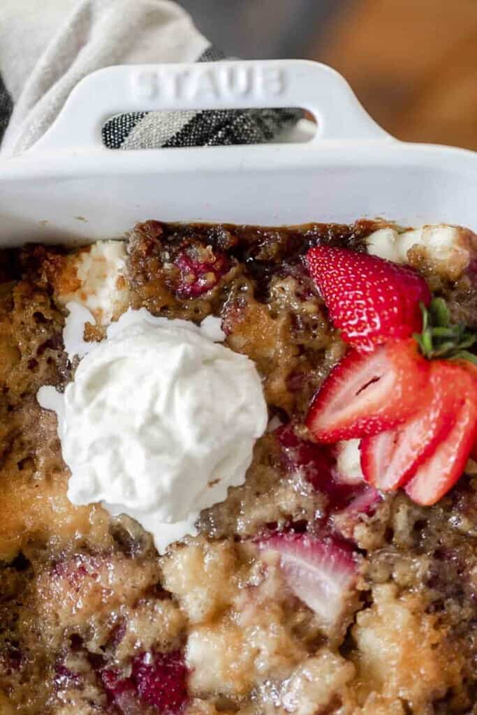 overhead photo of half of a sourdough strawberry cream cheese cobbler topped with strawberries and whipped cream in a white baking dish