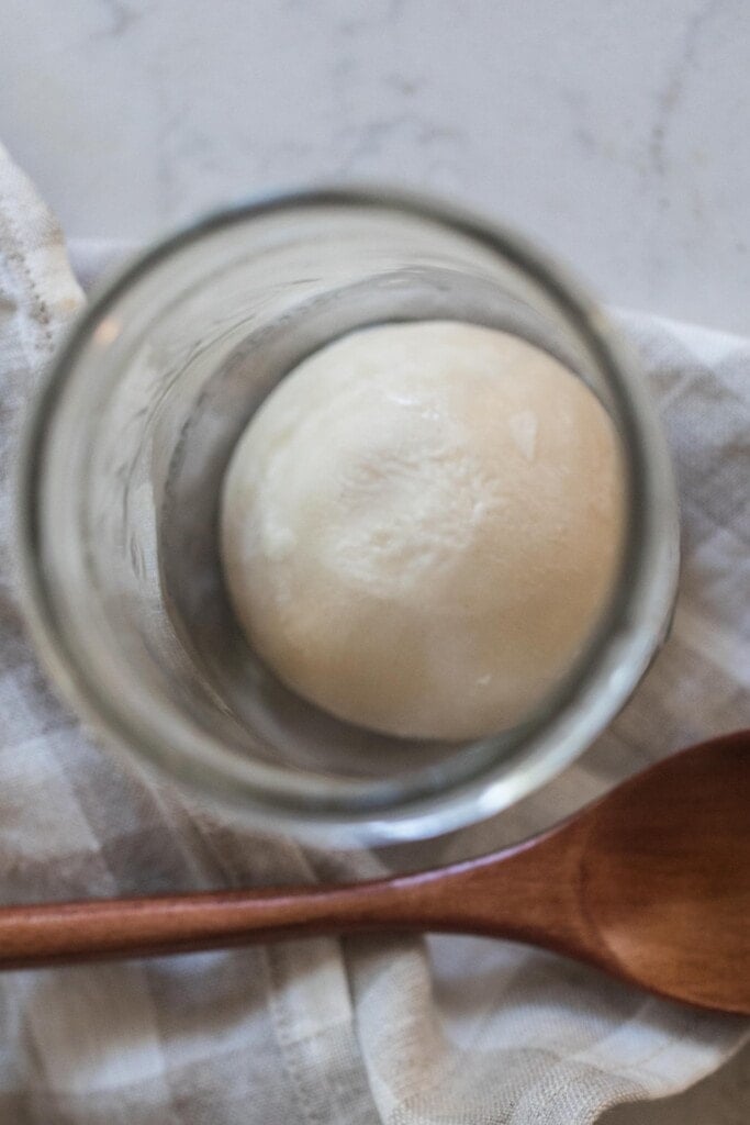 overhead photo of a frozen sourdough starter in a glass jar with a wooden spoon in front of the jar