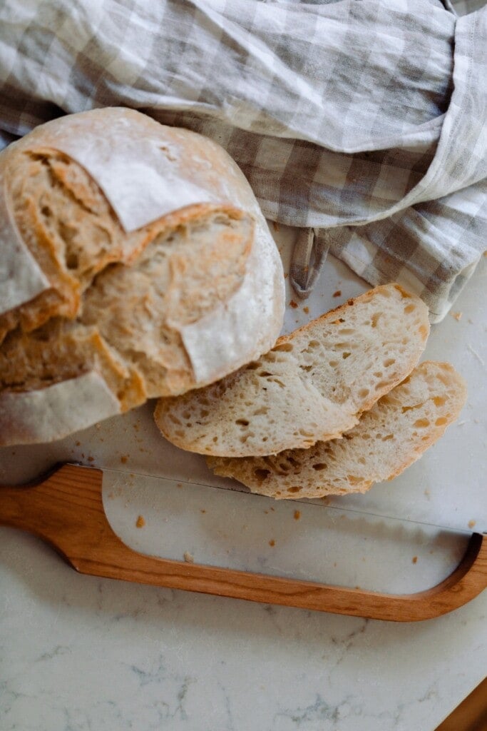 loaf of sourdough bread with two slices off and a knife laying on a white countertop